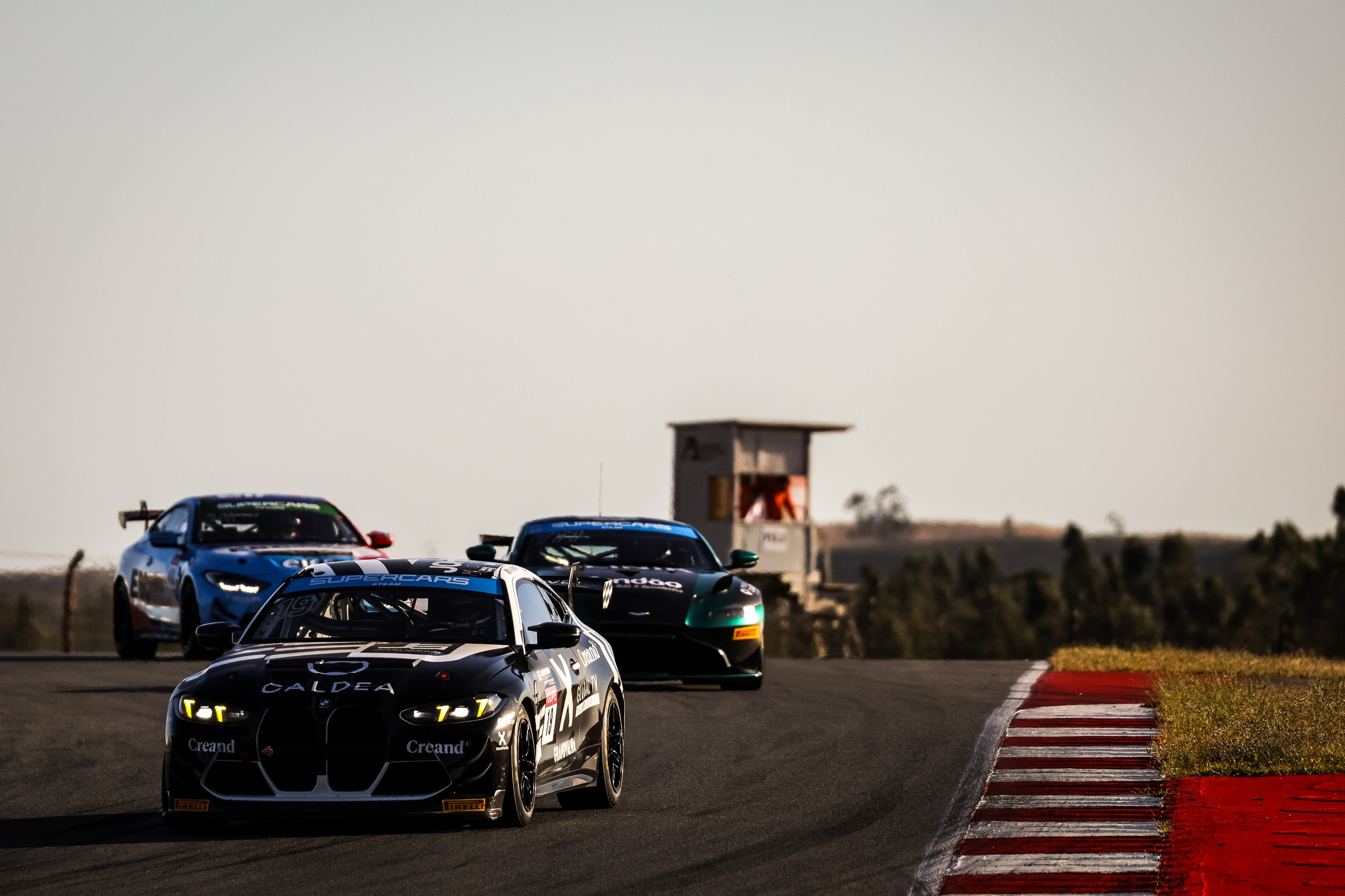 Três automóveis GT4 em corrida num circuito